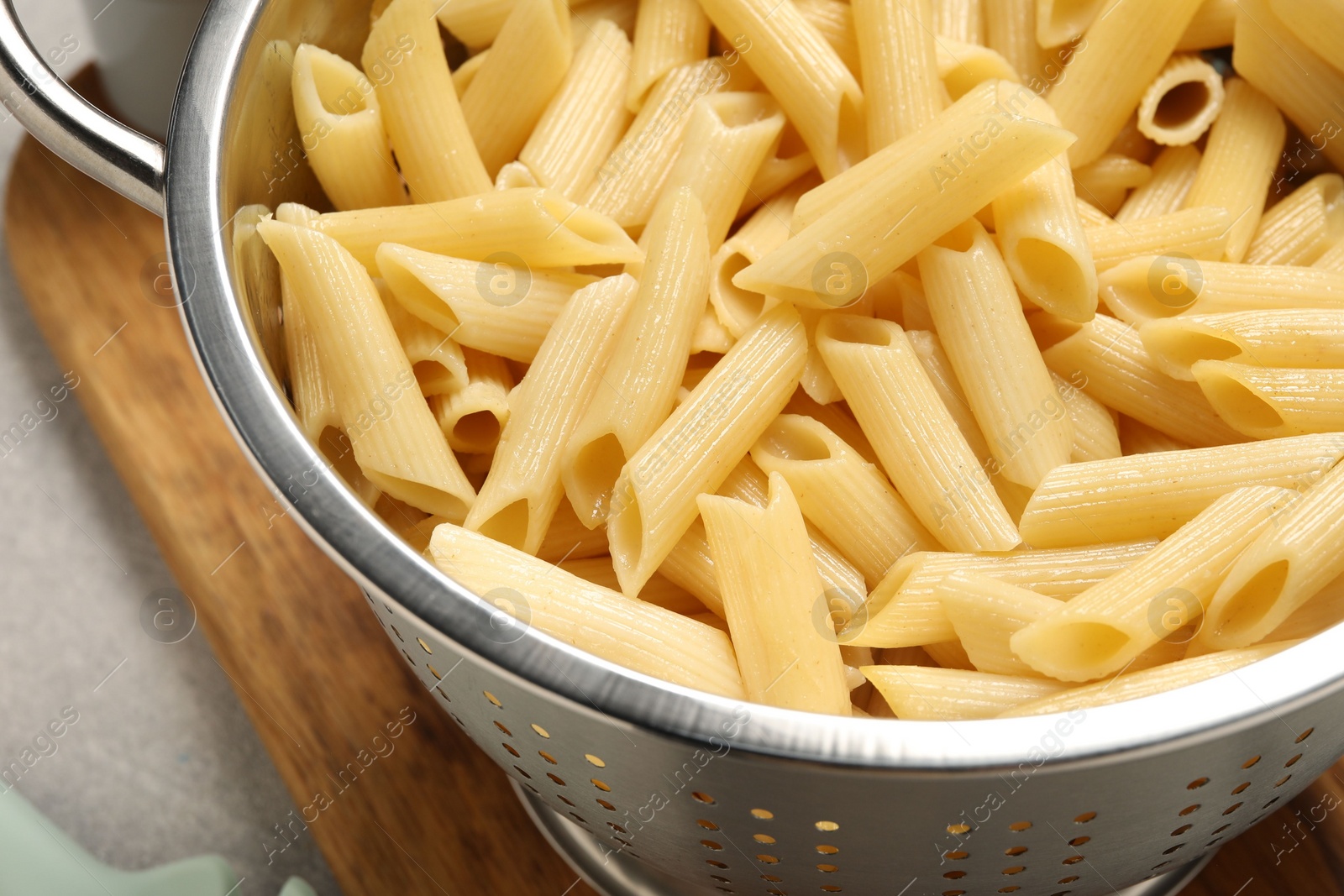 Photo of Delicious penne pasta in colander on table, closeup