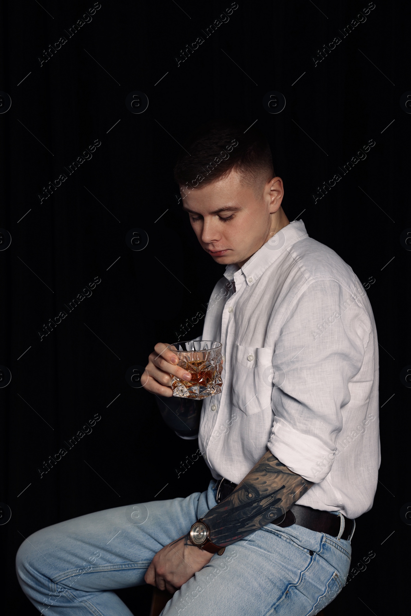 Photo of Young man with tattoos and glass of whiskey on dark background