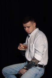 Photo of Young man with tattoos and glass of whiskey on dark background