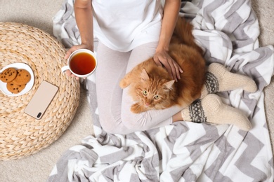 Photo of Woman with cute red cat and tea on blanket, top view