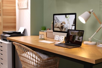 Photo of Stylish workplace with computer, laptop and lamp near olive wall at home