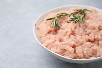 Photo of Fresh raw minced meat and rosemary in bowl on light grey textured table, closeup. Space for text