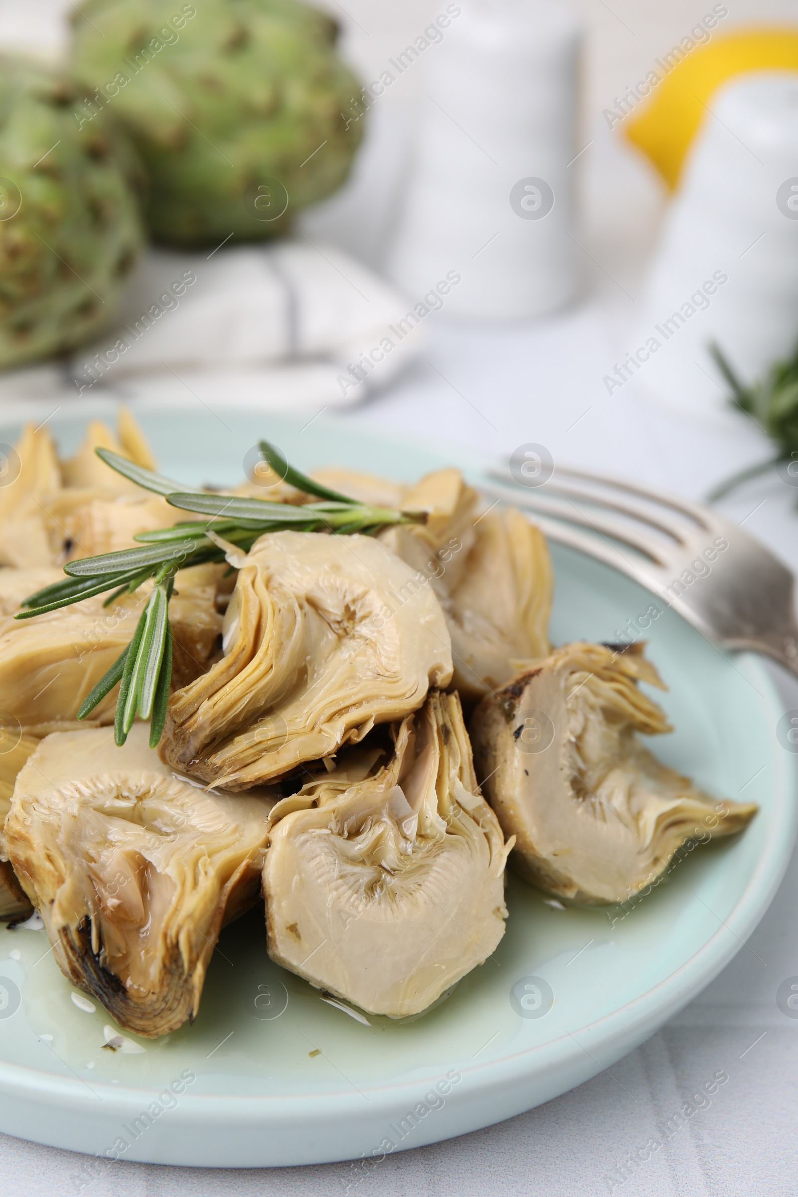 Photo of Plate with pickled artichokes and rosemary on white tiled table, closeup