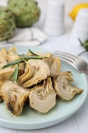 Plate with pickled artichokes and rosemary on white tiled table, closeup