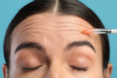 Photo of Young woman getting facial injection on light blue background, closeup. Cosmetic surgery