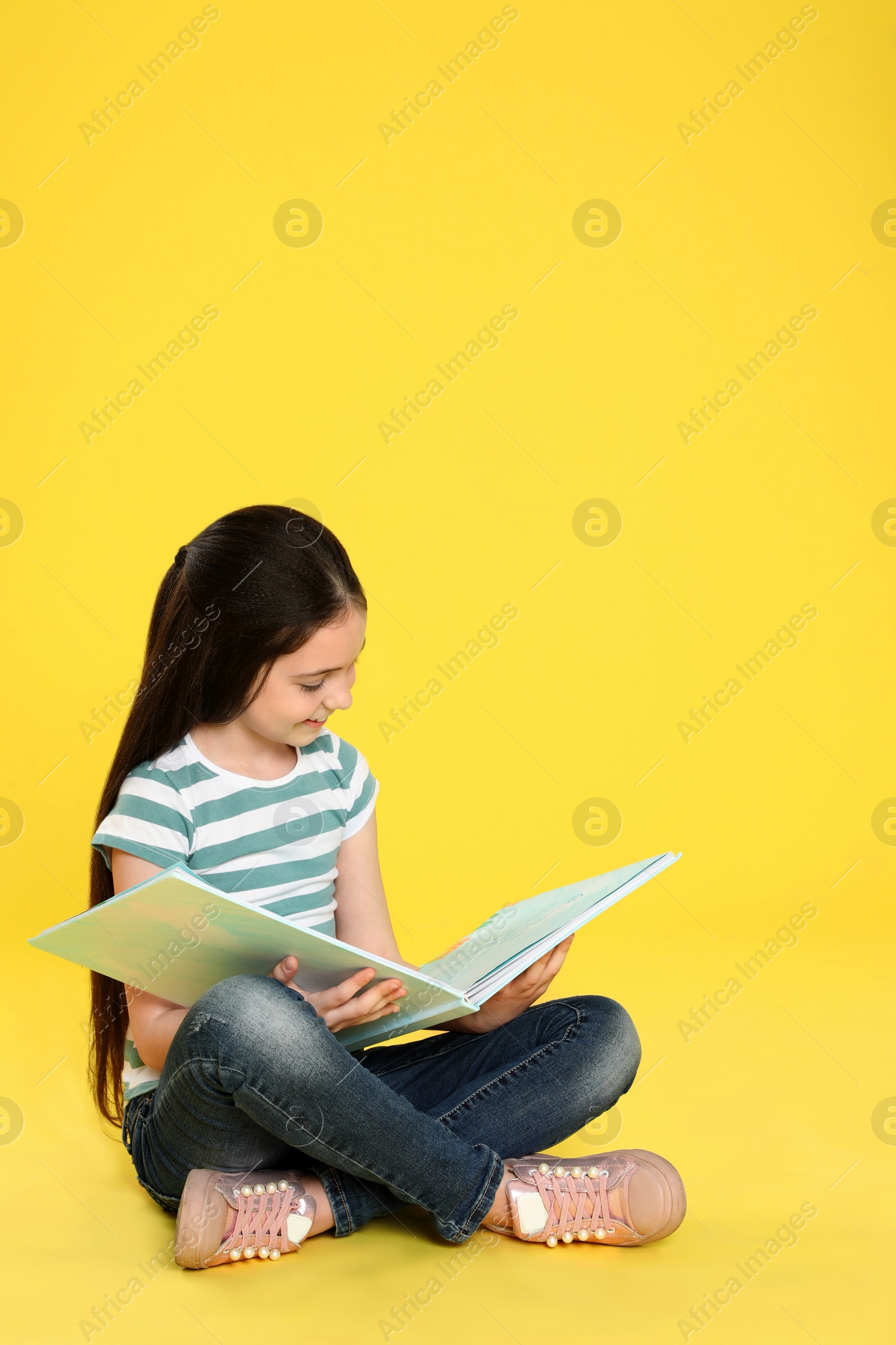 Photo of Cute little girl reading book on color background, space for text