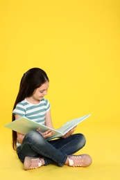 Cute little girl reading book on color background, space for text