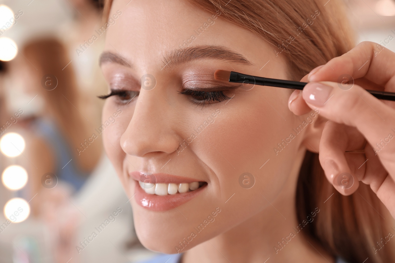 Photo of Professional makeup artist working with beautiful woman in salon