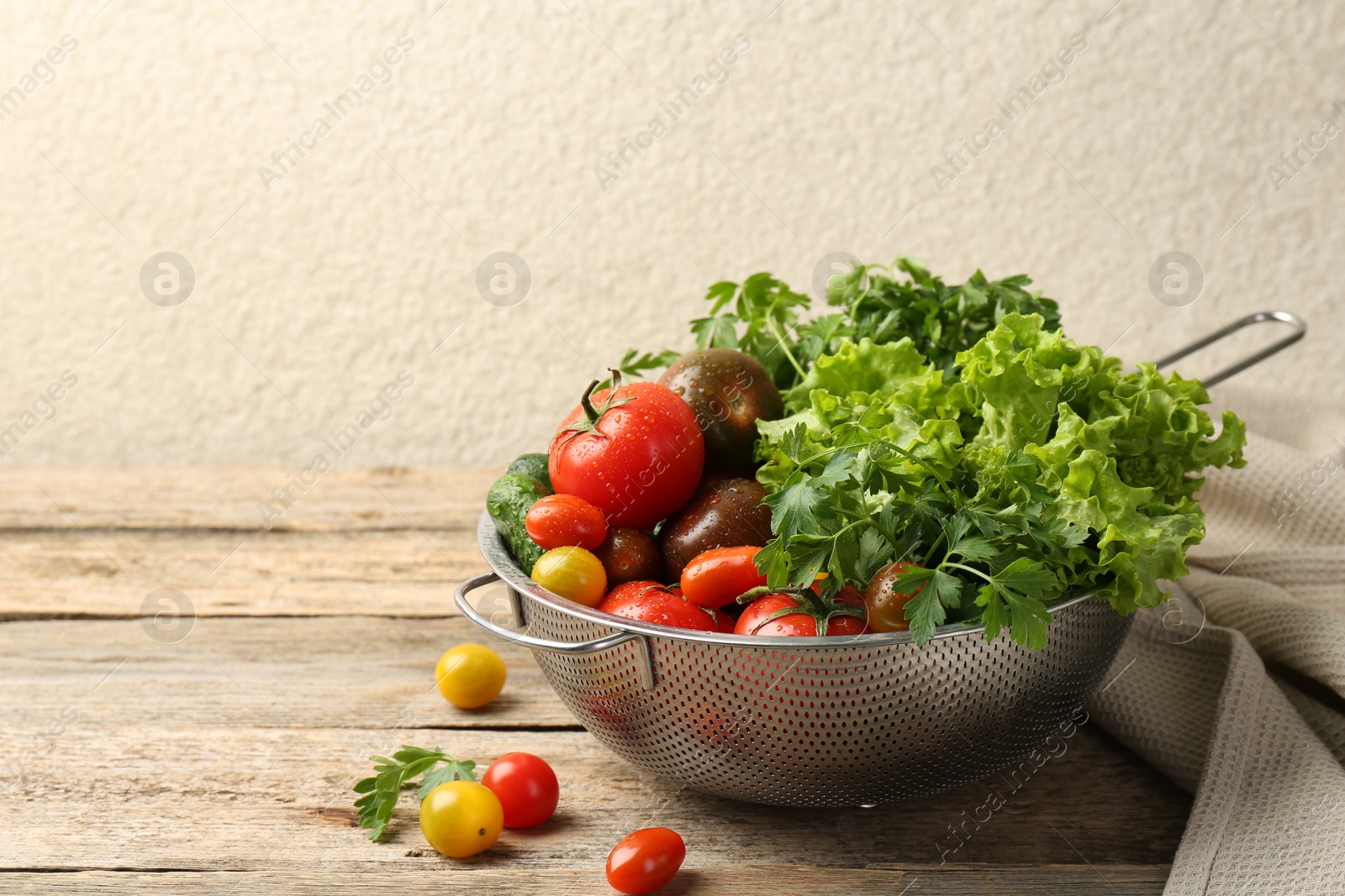 Photo of Wet vegetables in colander on wooden table, closeup. Space for text