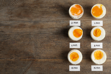 Photo of Different cooking time and readiness stages of boiled chicken eggs on wooden table, flat lay. Space for text
