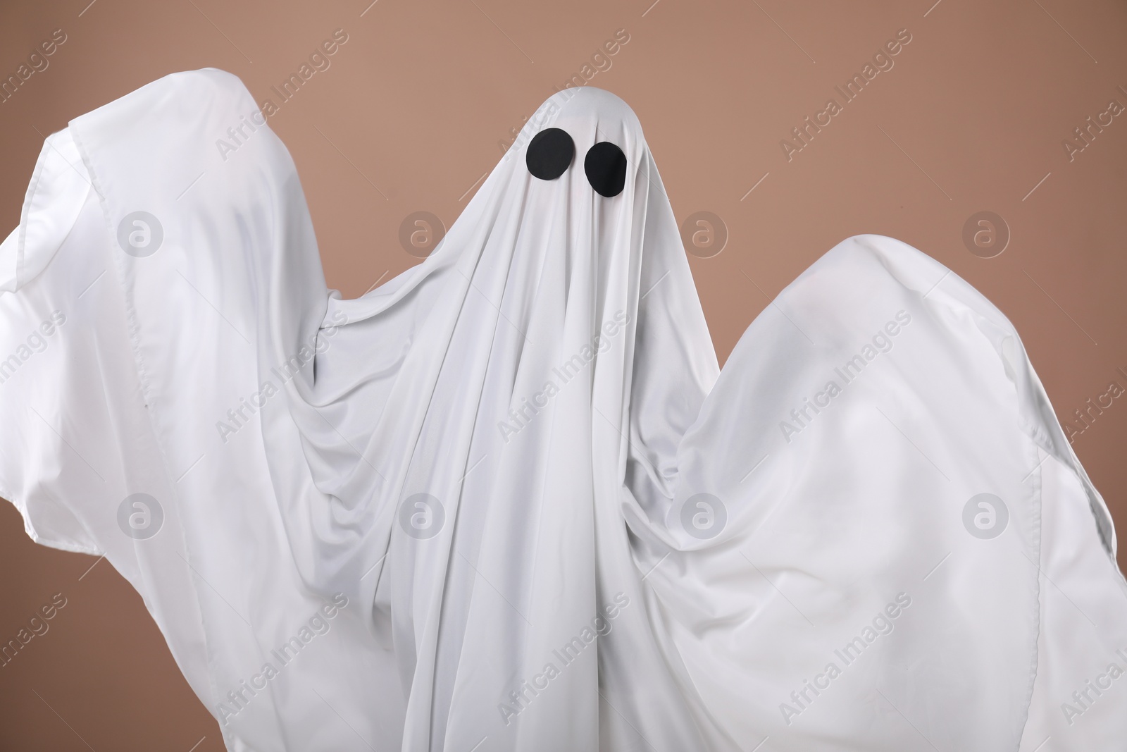 Photo of Creepy ghost. Person covered with white sheet on dark beige background