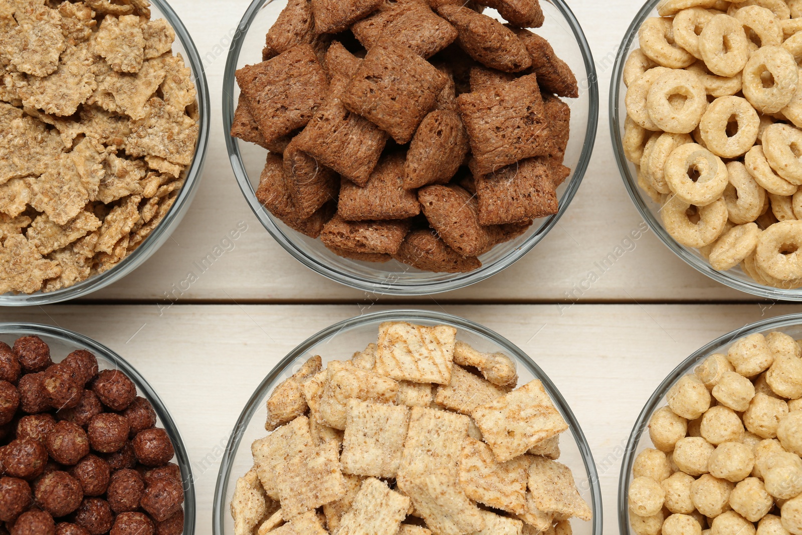 Photo of Different breakfast cereals in glass bowls on white wooden table, flat lay