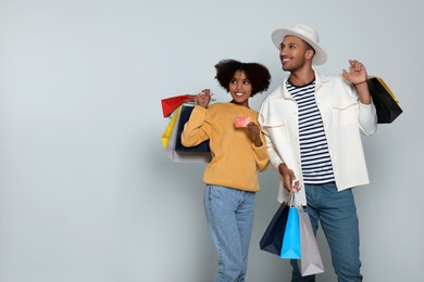 Photo of Happy African American couple with shopping bags and credit card on light grey background. Space for text
