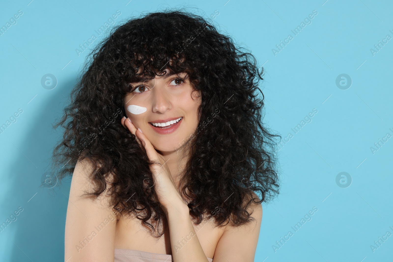 Photo of Beautiful young woman with sun protection cream on her face against light blue background