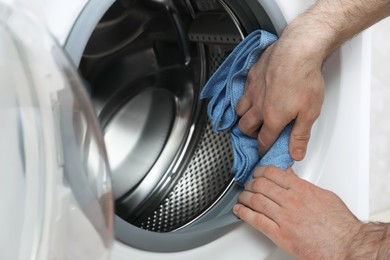 Photo of Man cleaning empty washing machine with rag, closeup