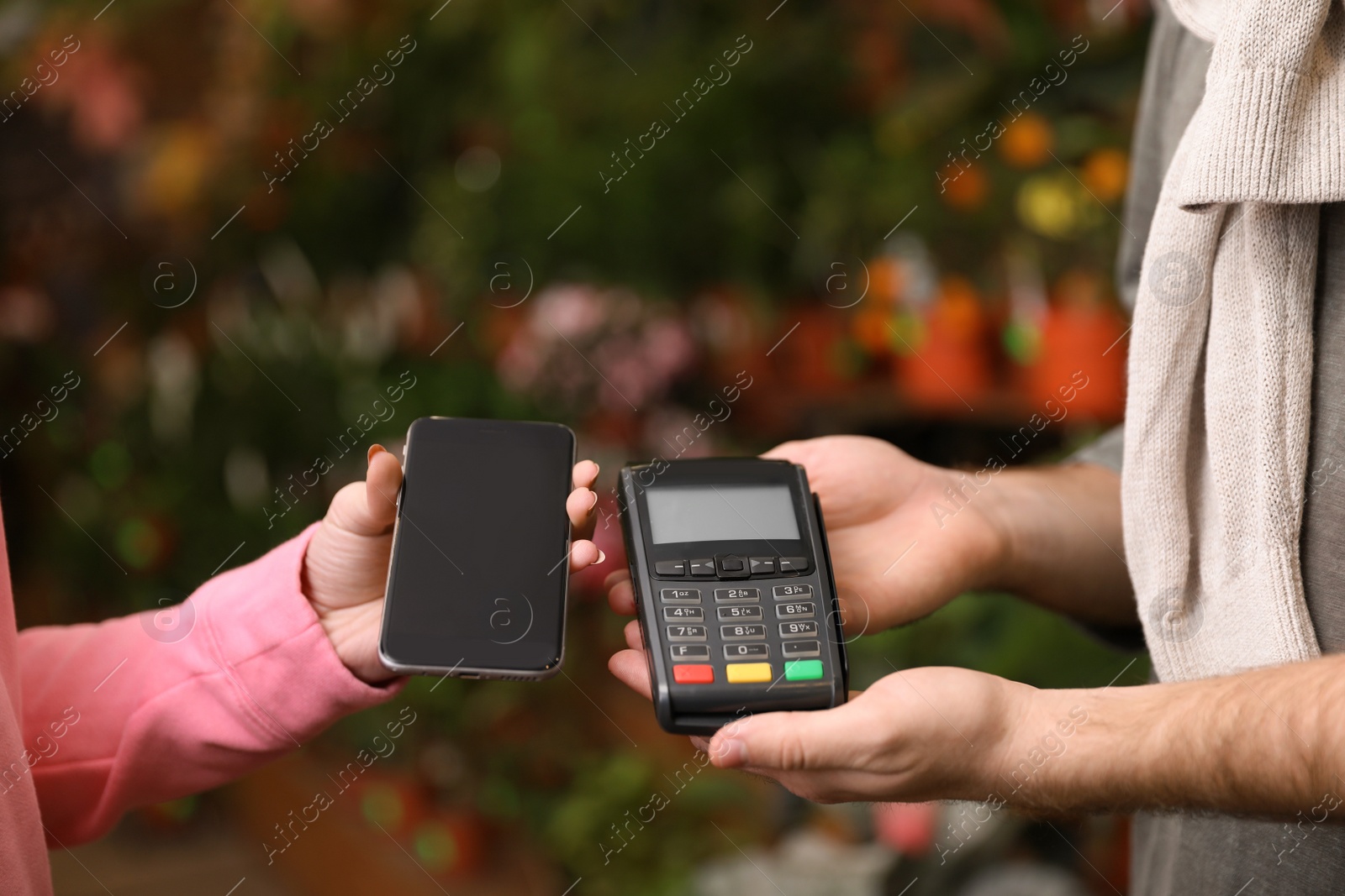 Photo of Woman using terminal for contactless payment with smartphone in floral shop, closeup. Space for text