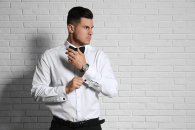 Handsome stylish man putting on cufflink near white brick wall. Space for text