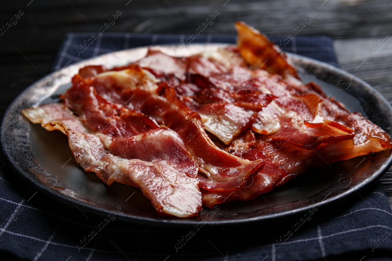 Photo of Slices of tasty fried bacon on black wooden table, closeup