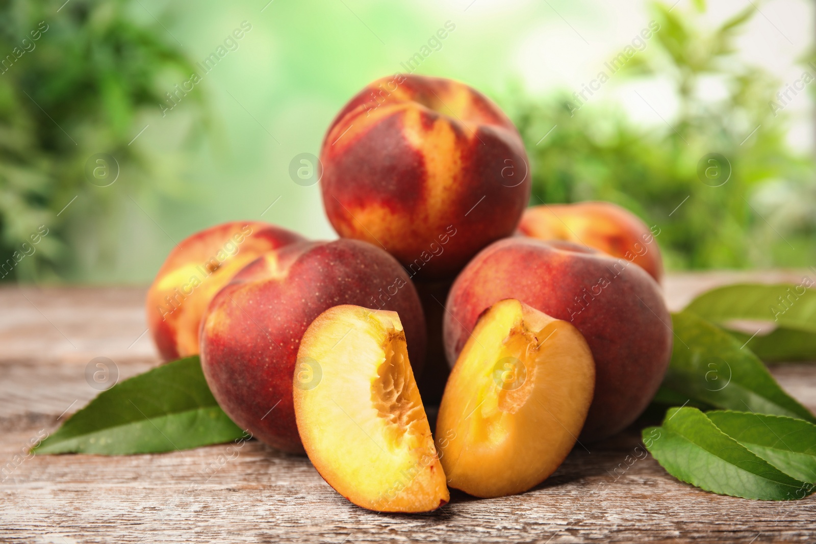 Photo of Fresh juicy peaches and leaves on wooden table against green blurred background