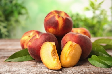 Fresh juicy peaches and leaves on wooden table against green blurred background