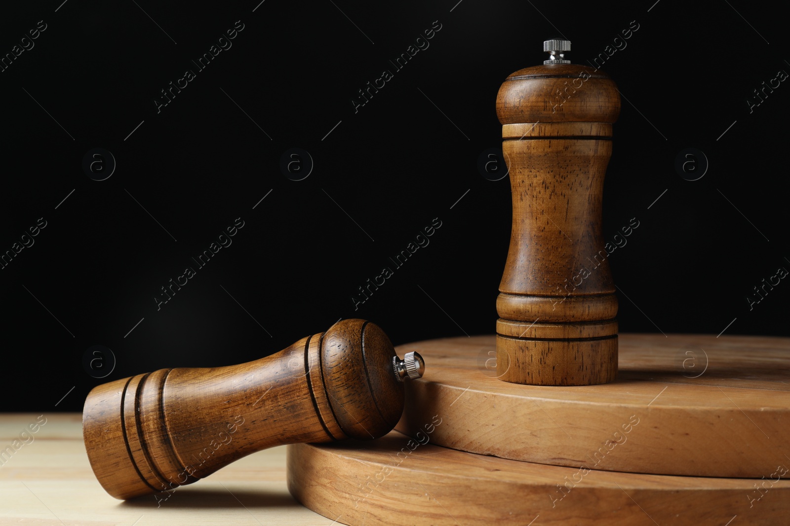 Photo of Salt and pepper shakers on wooden table against black background, closeup