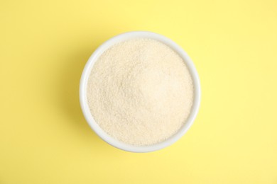 Photo of Gelatin powder in bowl on yellow background, top view