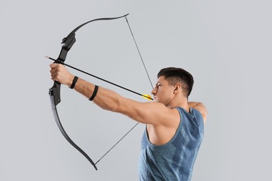 Photo of Man with bow and arrow practicing archery on light grey background