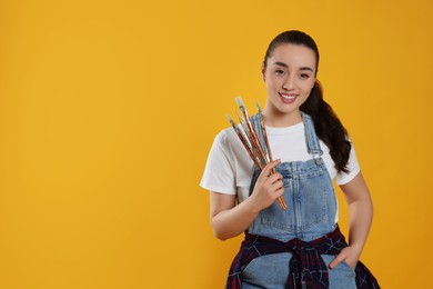 Photo of Woman with paintbrushes on yellow background, space for text. Young artist