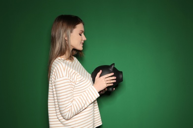 Young woman with piggy bank on color background. Space for text