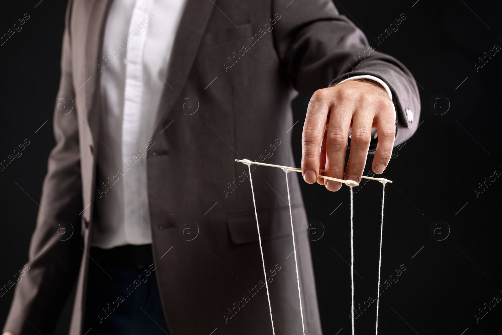 Photo of Man in suit pulling strings of puppet on black background, closeup