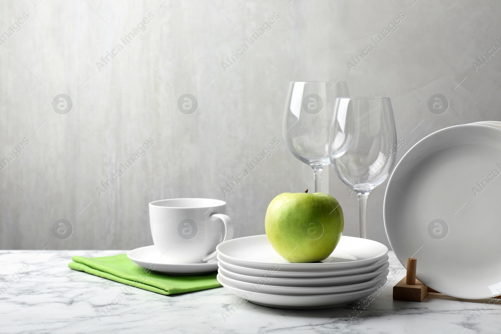 Photo of Set of clean dishware, glasses and apple on white marble table, space for text