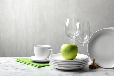 Photo of Set of clean dishware, glasses and apple on white marble table, space for text