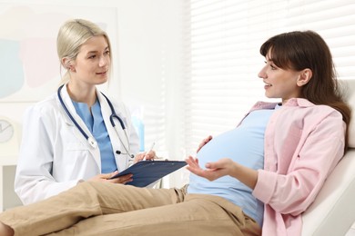 Photo of Doctor with clipboard consulting smiling pregnant patient in clinic