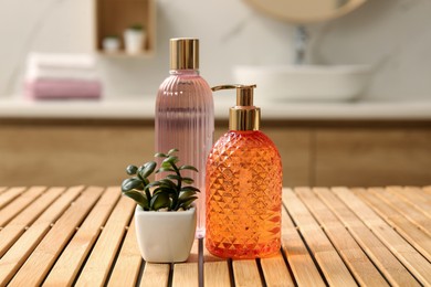 Glass dispenser with liquid soap, bottle of gel and plant on wooden table in bathroom