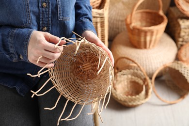 Photo of Woman weaving wicker basket indoors, closeup view