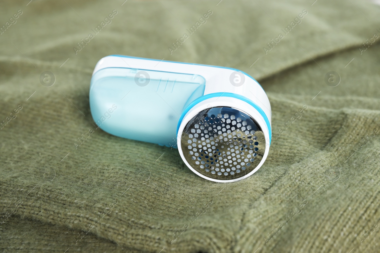 Photo of Modern fabric shaver device on olive cloth, closeup