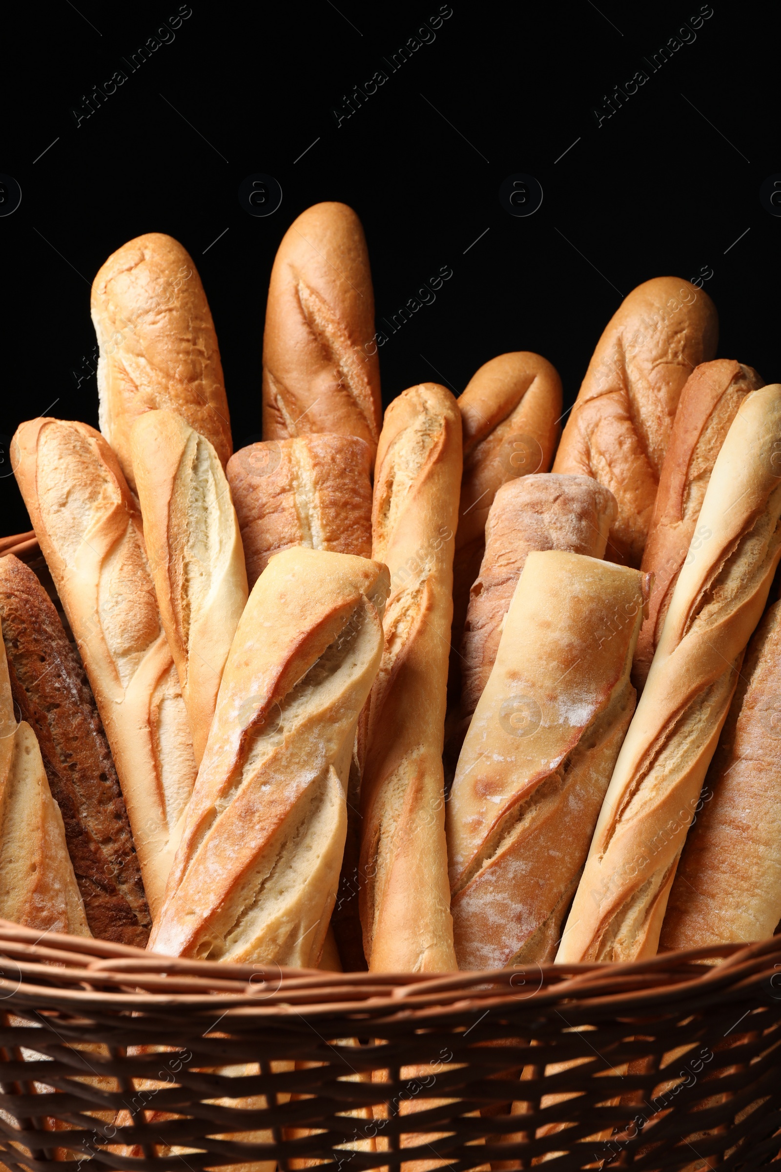 Photo of Fresh tasty baguettes in basket against black background, closeup