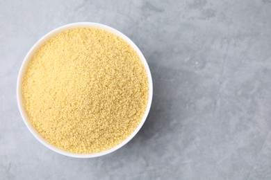 Raw couscous in bowl on gray table, top view. Space for text