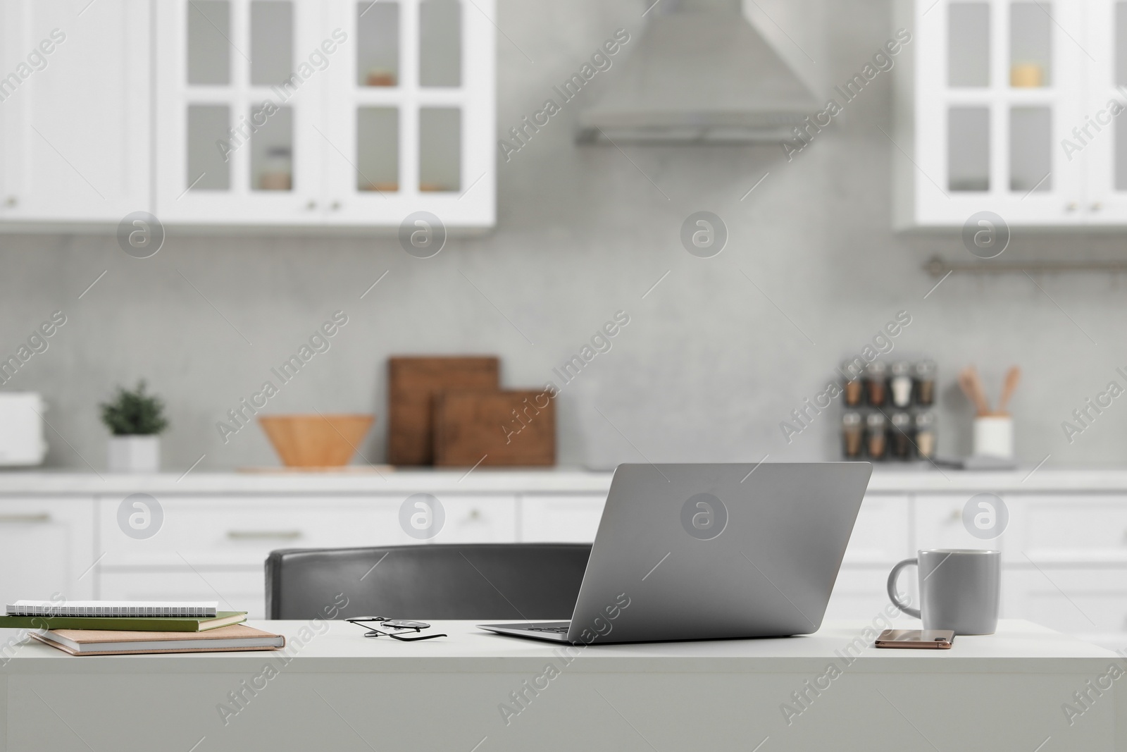 Photo of Home office. Laptop, glasses, smartphone and cup on white desk in kitchen, space for text