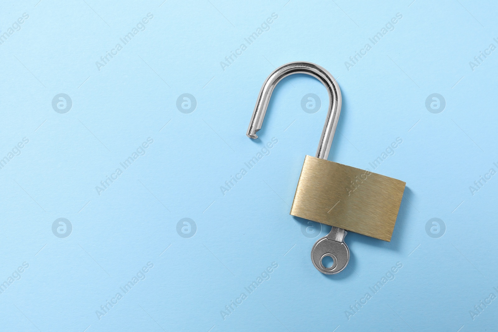 Photo of Steel padlock with key on light blue background, top view. Space for text