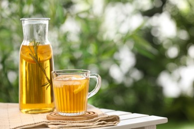 Photo of Glass bottle and cup of tasty iced tea on white table against blurred background, space for text