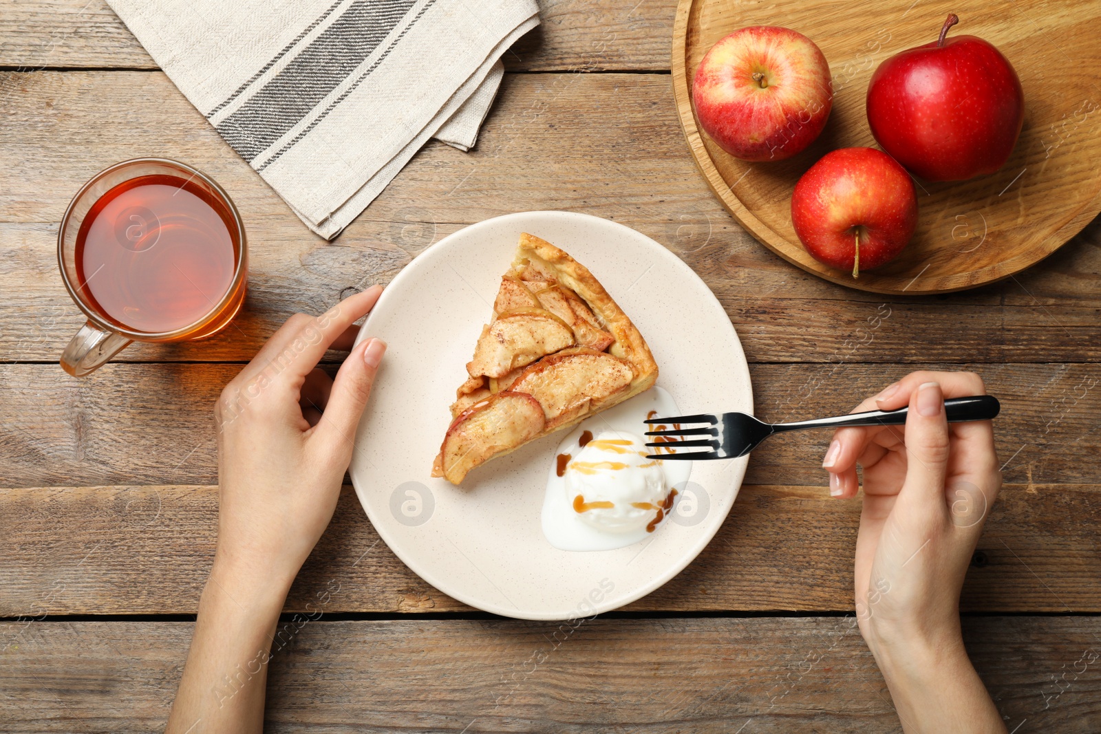 Photo of Woman eating delicious apple pie with ice cream at wooden table, top view