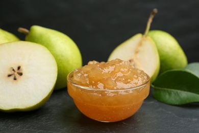 Photo of Tasty homemade pear jam and fresh fruits on black table