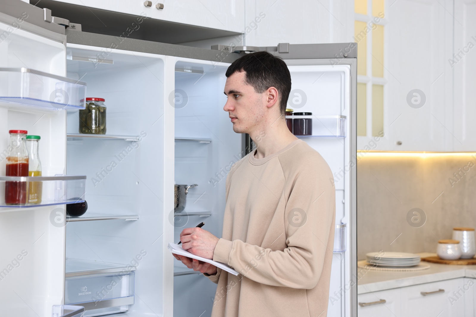 Photo of Man writing notes near empty refrigerator in kitchen