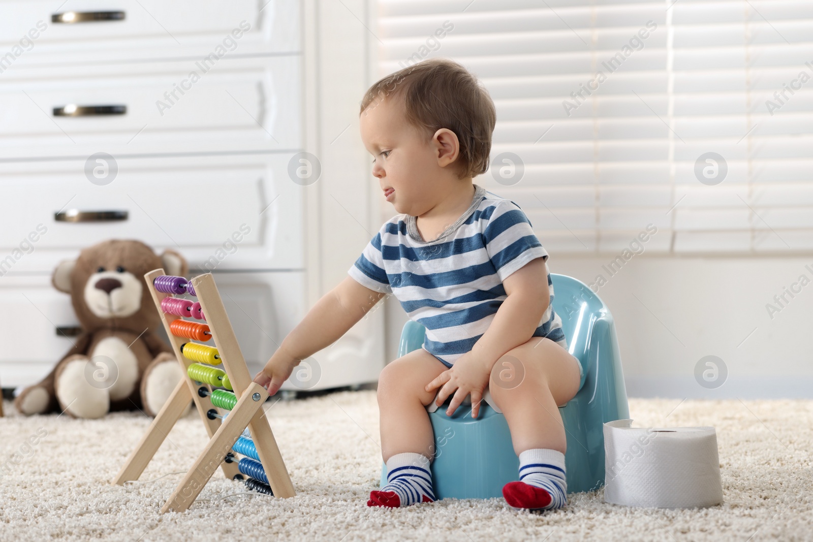 Photo of Little child with abacus sitting on plastic baby potty indoors