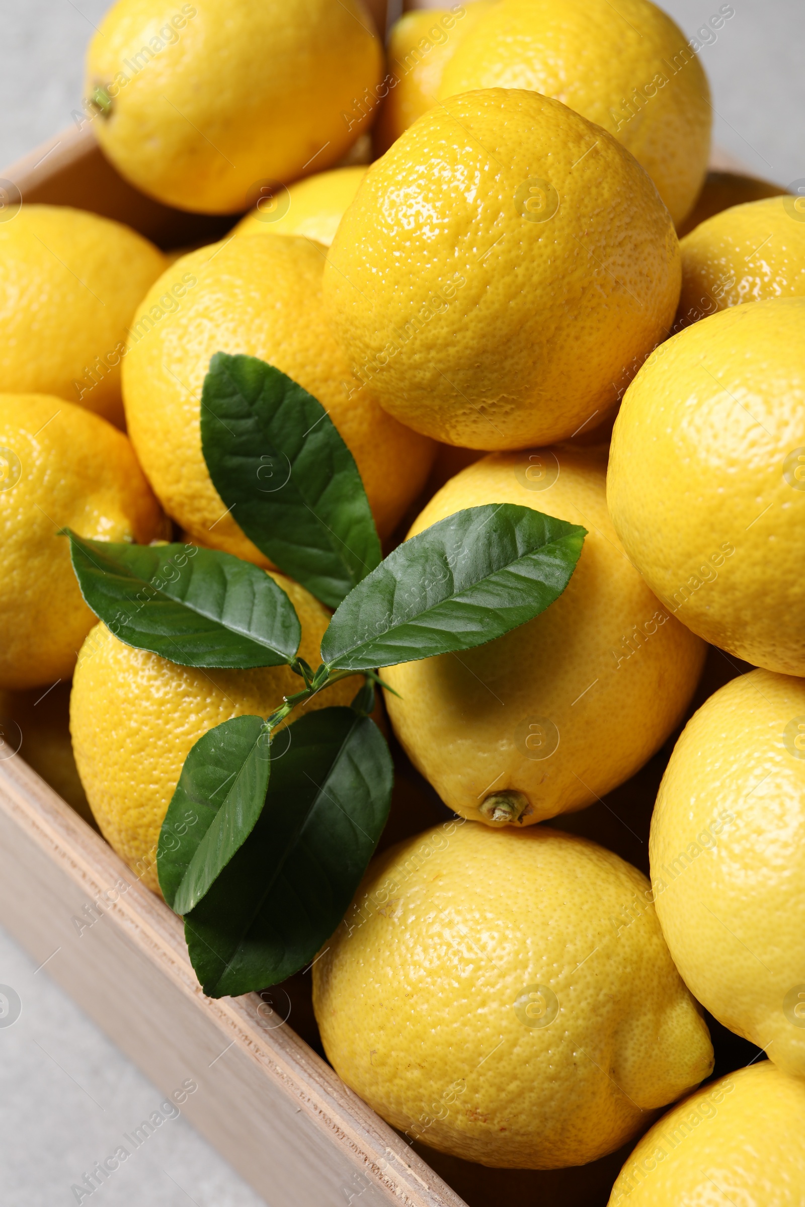Photo of Fresh lemons in wooden crate on grey table, closeup