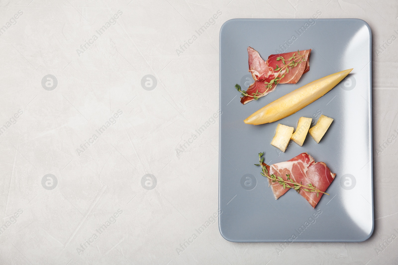 Photo of Plate of melon slices and prosciutto on gray background, top view. Space for text