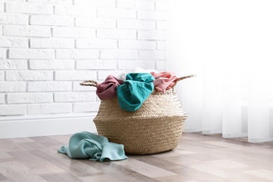 Photo of Wicker basket with dirty laundry on floor near window
