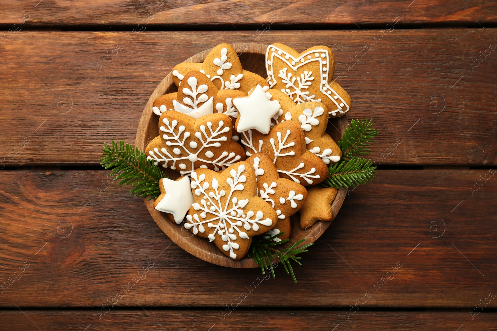 Photo of Tasty Christmas cookies with icing and fir tree branches in bowl on wooden table, top view