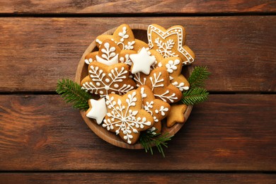 Photo of Tasty Christmas cookies with icing and fir tree branches in bowl on wooden table, top view